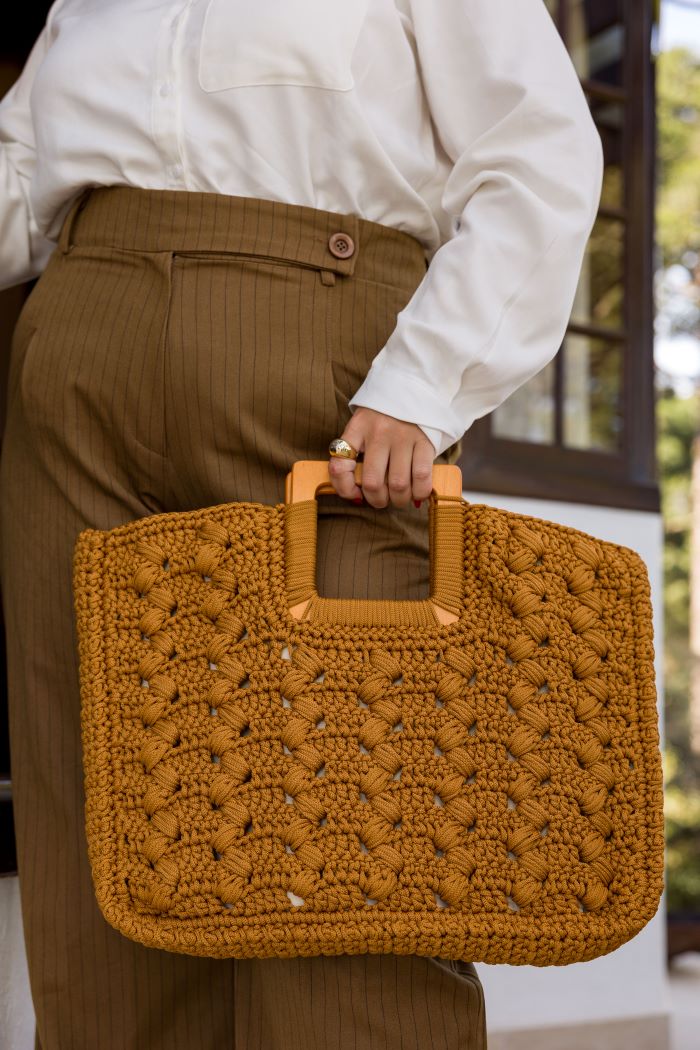 Circulo Fio Náutico Poly 5 mm – Polyester Cord Yarn ( 178 m  / 500 g) - A person wearing a white button-up shirt and brown pinstriped trousers holds a large, textured mustard-yellow crocheted tote bag with tan handles.